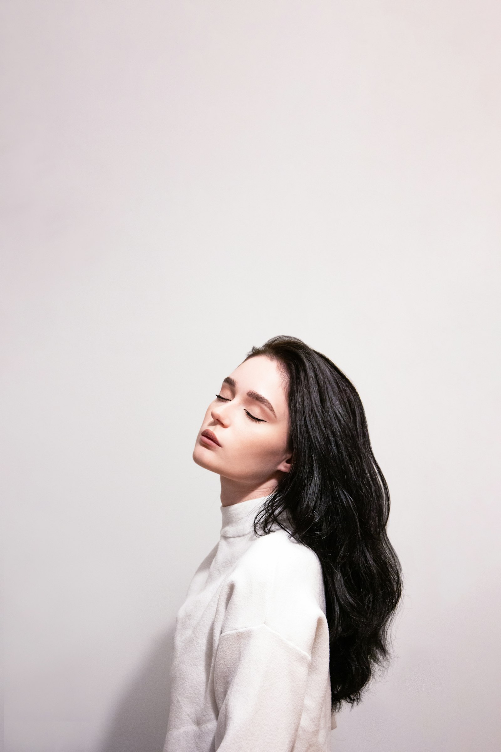 白い壁を背に、黒髪のロングヘアをなびかせる女性